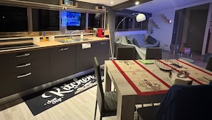 A modern kitchen with a built-in TV, a dining area with a table set for two, and a staircase leading to a living area.