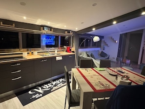 A modern kitchen with a built-in TV, a dining area with a table set for two, and a staircase leading to a living area.