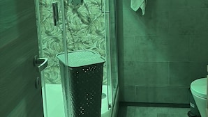 A glass-enclosed shower with a floral pattern on the wall, a towel hanging on the wall, and a toilet visible in the corner.