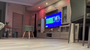 A modern living room with a flat-screen TV, a clock, and a small stool.