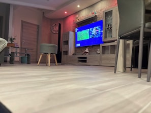 A modern living room with a flat-screen TV, a clock, and a small stool.