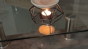 A glass table with a candle in a geometric holder, a wooden crate labeled 'STORE ACE BOX' in the background, and a 'TEMPERED GLASS' sign on the table.
