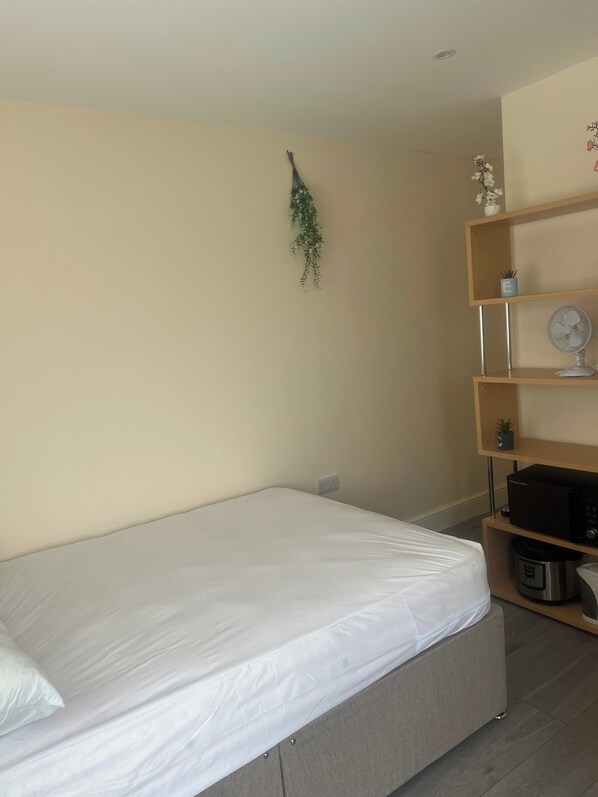 Un dormitorio con una cama, un estante con un ventilador y una planta pequeña.