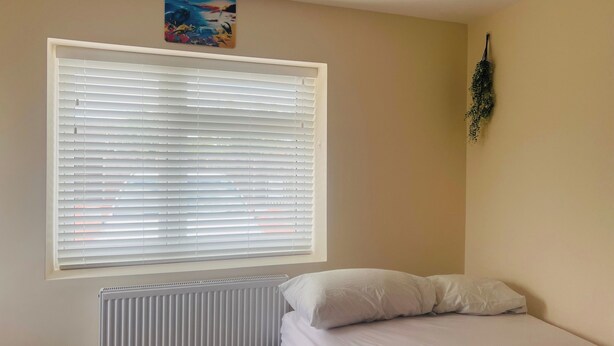 Un dormitorio con cama, un radiador, una ventana con persianas y un adorno en la pared.