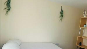 Un dormitorio con una cama, un estante de madera con una planta pequeña y una planta colgante en la pared.