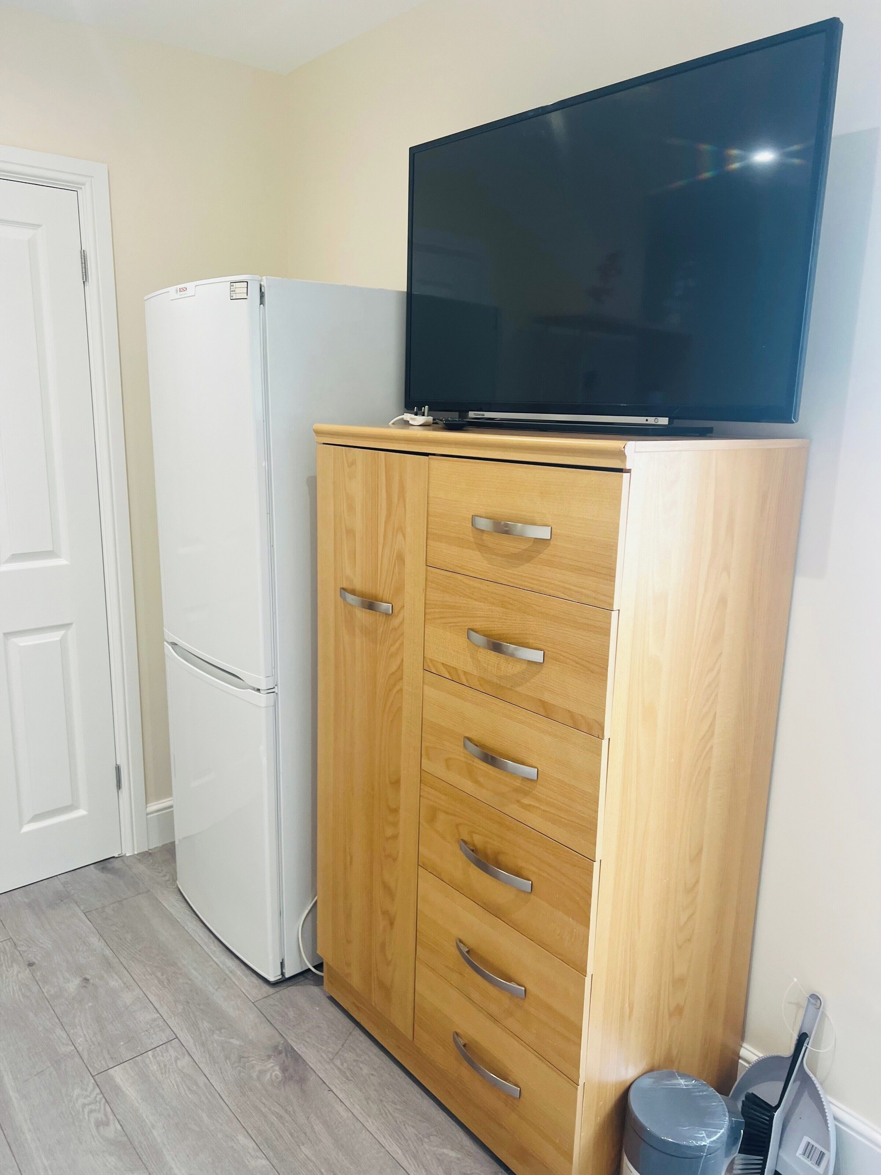 Una kitchenette con un refrigerador blanco, un gabinete de madera con cajones y un televisor de pantalla plana montado encima.