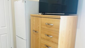 Una kitchenette con un refrigerador blanco, un gabinete de madera con cajones y un televisor de pantalla plana montado encima.