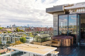 Une terrasse sur le toit avec une table, un jacuzzi et un espace clos par des baies vitrées offrant une vue sur la ville.