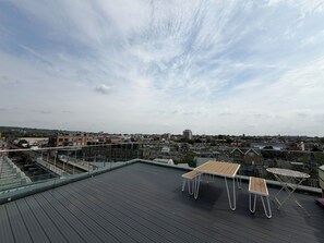 A rooftop terrace with a table and chairs, overlooking a cityscape with buildings and a river. - Stunning 2BDR Flat w Skyline Views in Kentish Town (Greater London)