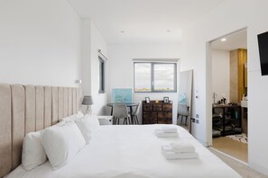A hotel room with a bed, a desk, a chair, and a view of the city. - Stunning 2BDR Flat w Skyline Views in Kentish Town (Greater London)