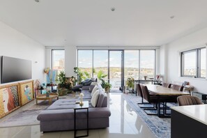 A modern living room with a sofa, dining table, and large windows offering a city view. - Stunning 2BDR Flat w Skyline Views in Kentish Town (Greater London)