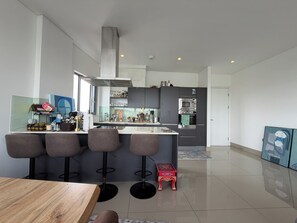 A modern kitchen with a central island, bar stools, and a dining table. - Stunning 2BDR Flat w Skyline Views in Kentish Town (Greater London)