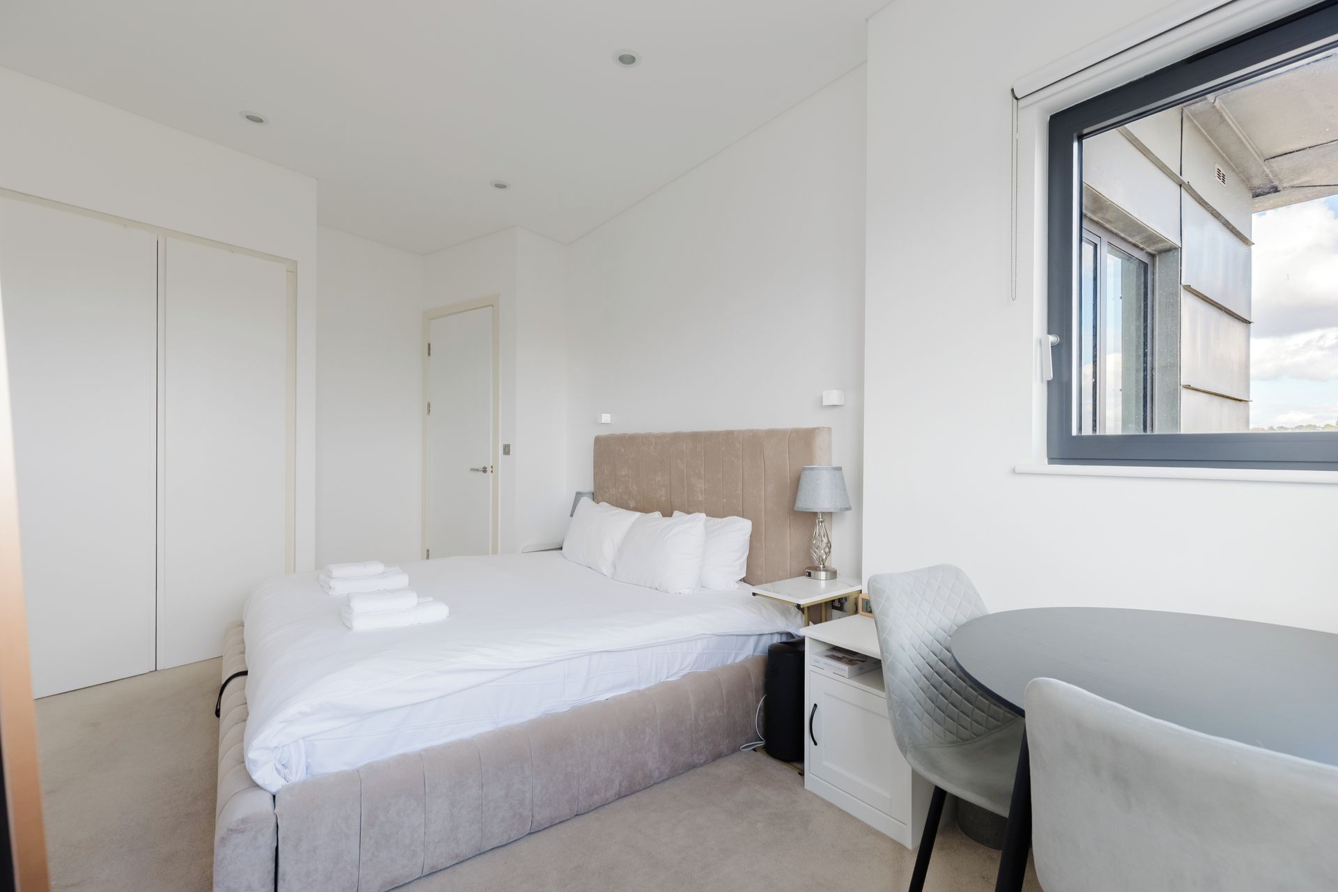A hotel room with a bed, a desk, a chair, a window, and a door.