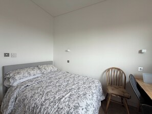 A bedroom with a bed, a chair, a desk, and a wall socket. - Stunning 2BDR Flat w Skyline Views in Kentish Town (Greater London)