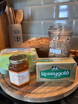 Uma tábua de madeira com um pote de marmelada, um pão, um pote de granola, um pote de geleia e uma caixa de manteiga irlandesa.