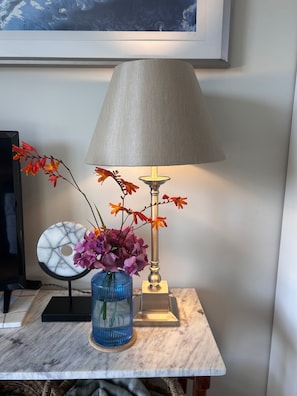 Uma mesa com uma lâmpada, um vaso com flores e um prato decorativo.