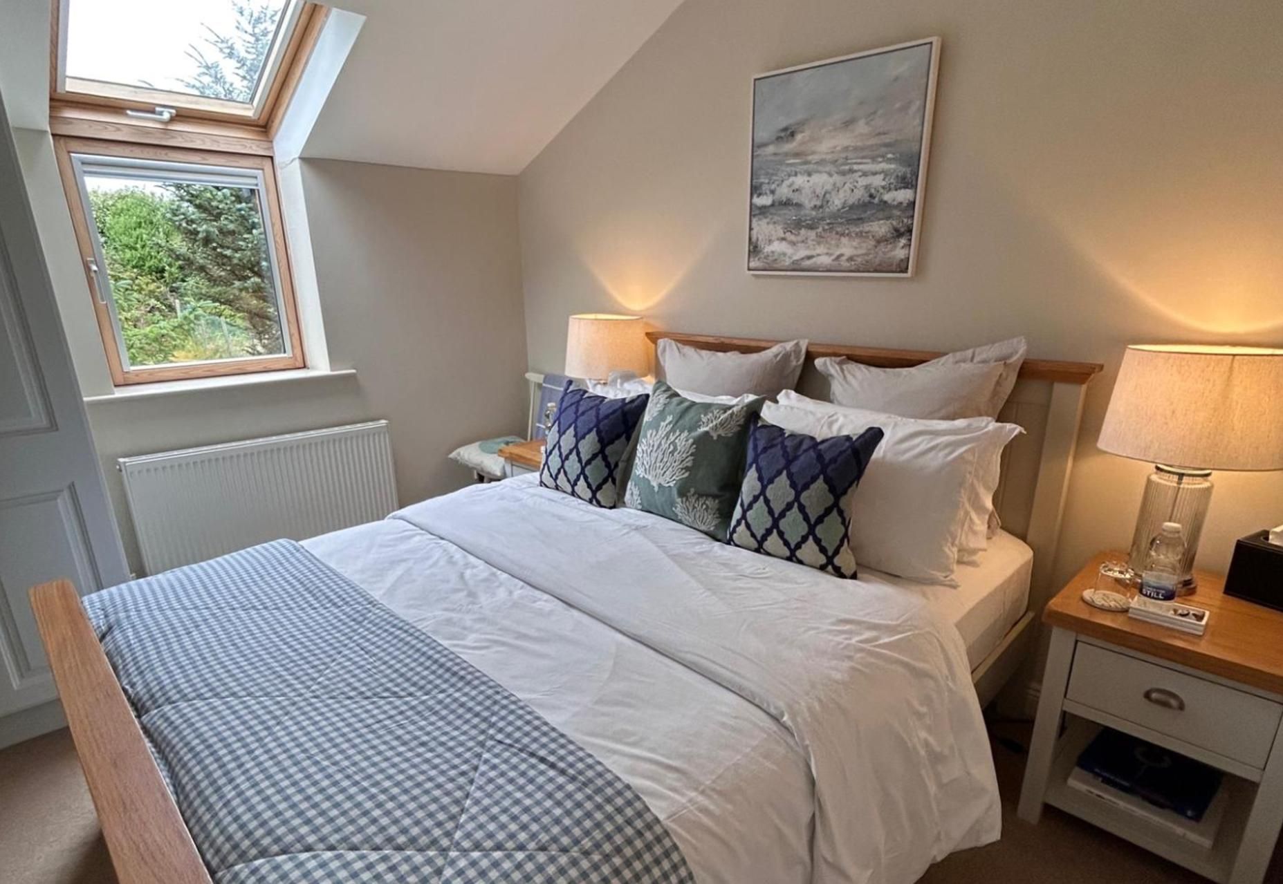 A bedroom with a bed, bedside tables, a nightstand, a window, and a painting on the wall.