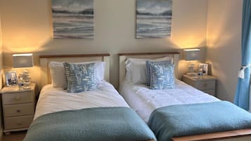 A double room with two beds, each with a nightstand, a lamp, and a small table. There are two wall-mounted paintings above the beds.