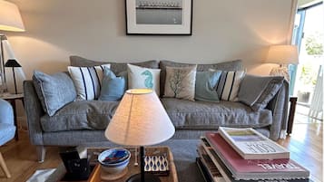 A living room with a grey sofa, a table with books, a bowl, and a lamp.