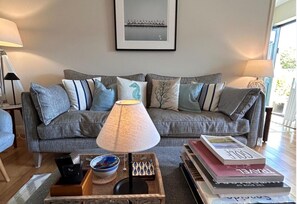 A living room with a grey sofa, a table with books, a bowl, and a lamp. - Waterville Village Retreat - Sleeps 6 - Wood Stove (Waterville)