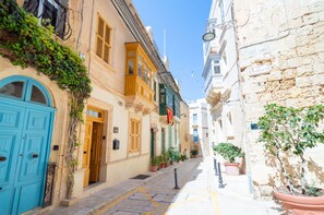 A narrow street with buildings on either side, featuring traditional architecture and potted plants. - Stylish traditional house with sun terrace TELL1-1 (Birgu)