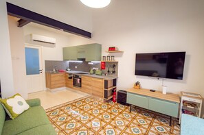 Un espacio habitable compacto con kitchenette, televisor y piso estampado.