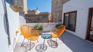 A balcony with two orange chairs and a blue table, a potted plant, and a view of a stone building. - Stylish traditional house with sun terrace TELL1-1 (Birgu)