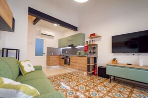 A compact living space with a kitchenette, a sofa with a pillow, a television, and a patterned floor. - Stylish traditional house with sun terrace TELL1-1 (Birgu)