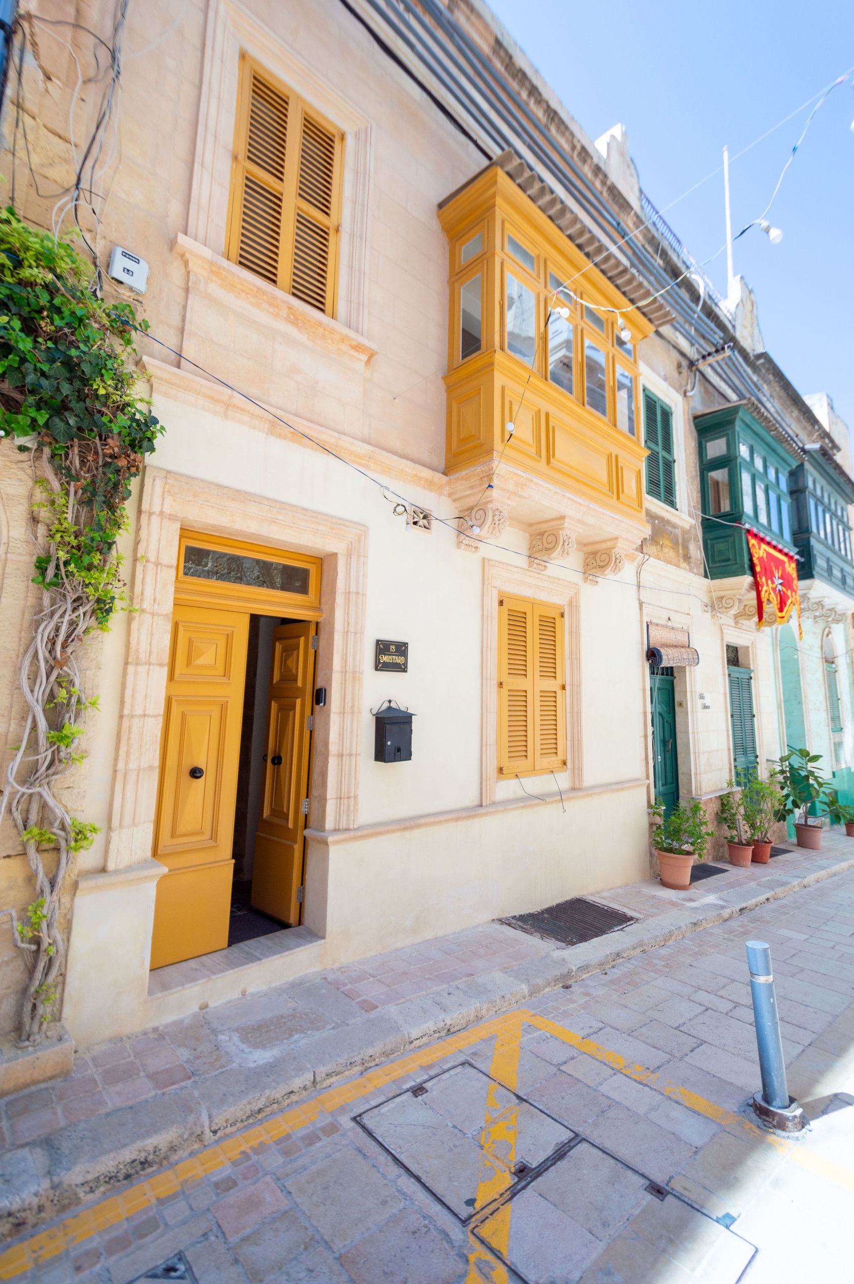 Un bâtiment avec une porte jaune, une fenêtre avec des volets et une enseigne sur laquelle on peut lire « 13 Mustard ».
