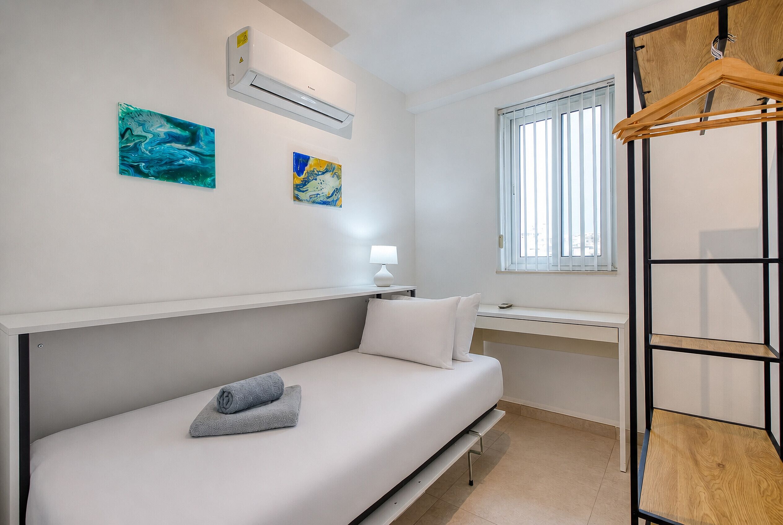 Un dormitorio pequeño con una cama individual, un escritorio y una ventana con persianas verticales.