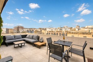 A rooftop terrace with a sofa set, a table, and chairs, overlooking a cityscape with buildings and construction cranes. - Beautiful penthouse with terrace & jacuzzi WVID1-2 (Msida)
