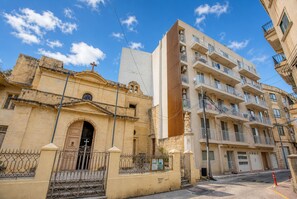 A historic church with a traditional facade and a modern apartment building with balconies and a vertical wooden panel. - Beautiful penthouse with terrace & jacuzzi WVID1-2 (Msida)