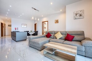 A modern living room with a grey sofa, a wooden coffee table, and a dining area with a white table and chairs. - Spacious & bright 3 bedroom with balcony KDEB1-1 (Marsaxlokk)