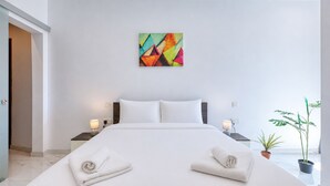 Ett modernt hotellrum med en stor säng, två sängbord med lampor, en färgstark, abstrakt målning på väggen och en krukväxt.
