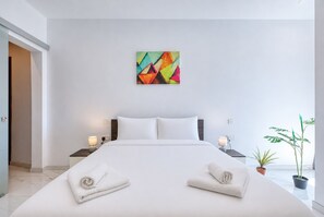 Ein modernes Hotelzimmer mit einem großen Bett, zwei Nachttischen mit Lampen, einem farbenfrohen abstrakten Gemälde an der Wand und einer Topfpflanze.