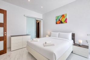 A modern hotel room with a large bed, a bedside table with a lamp, a wardrobe, and a colorful abstract painting on the wall. - Spacious & bright 3 bedroom with balcony KDEB1-1 (Marsaxlokk)