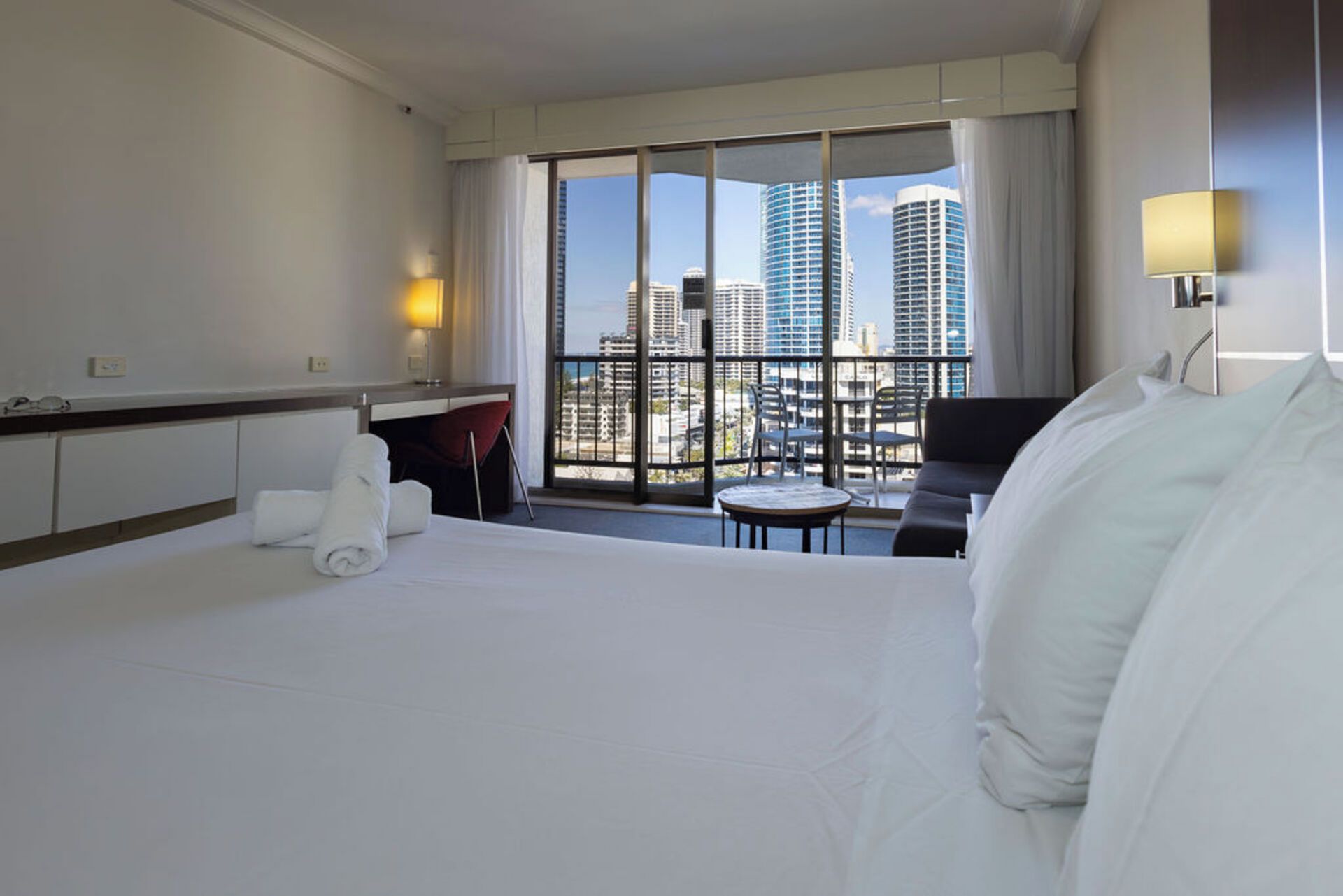 Une chambre d’hôtel équipée d’un lit, d’un bureau, d’une chaise et offrant une vue sur le paysage urbain grâce à de grandes fenêtres.