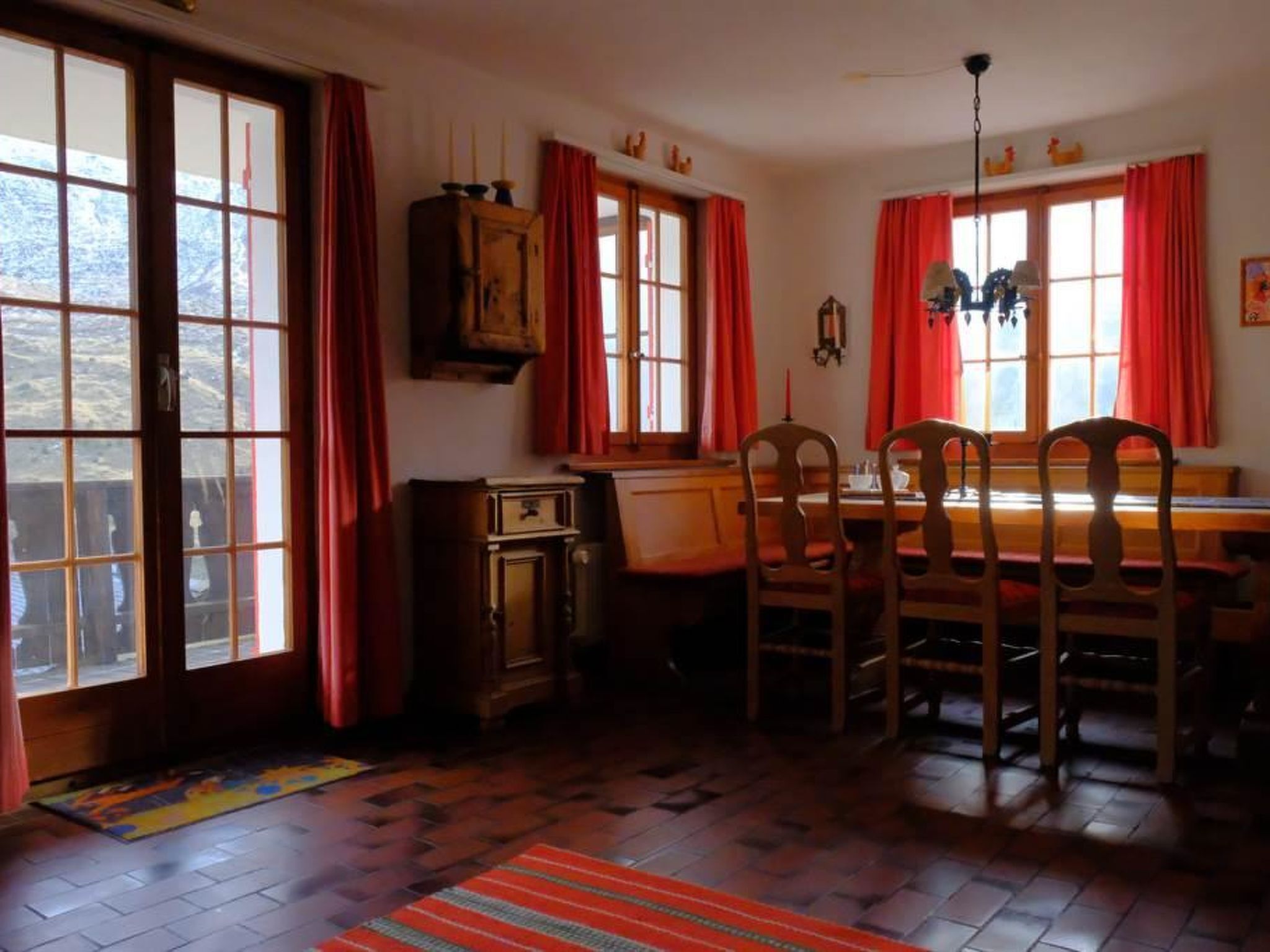 Et spiseområde med træstole, et bord og et vindue med røde gardiner.