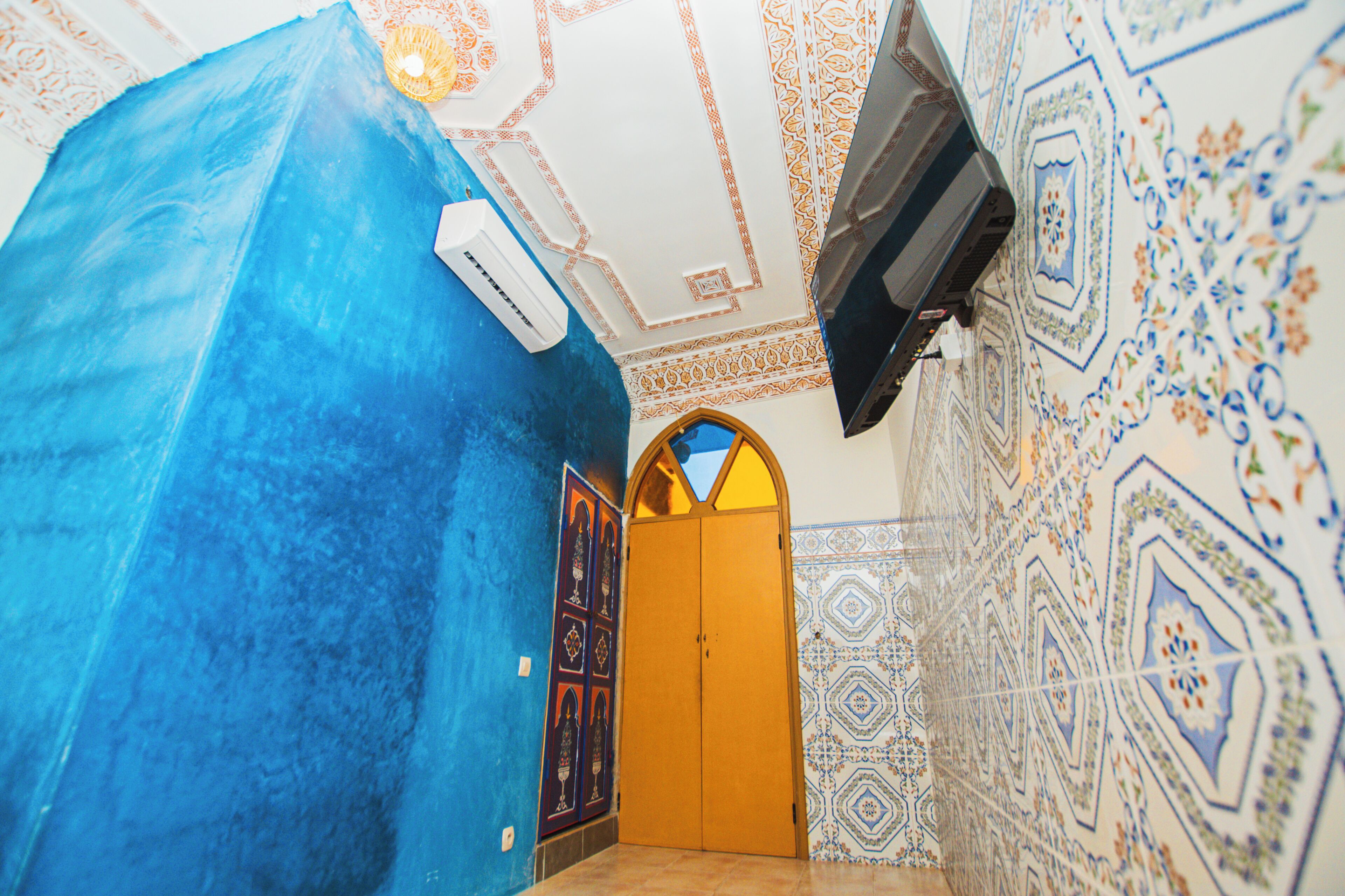 Een kamer met een blauwe wand, een wand met patroontegels, een houten deur en een plafond met decoratief ontwerp.