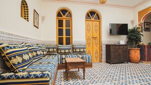 Quarto com sofá estampado, mesa de madeira e televisão.