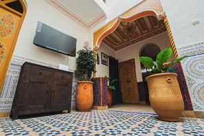 Decoração tradicional com televisão de tela plana na parede, um armário de madeira e grandes vasos de terracota com plantas.