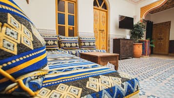 A room with a bed featuring patterned bedding, a wooden nightstand, a television mounted on the wall, and a potted plant.