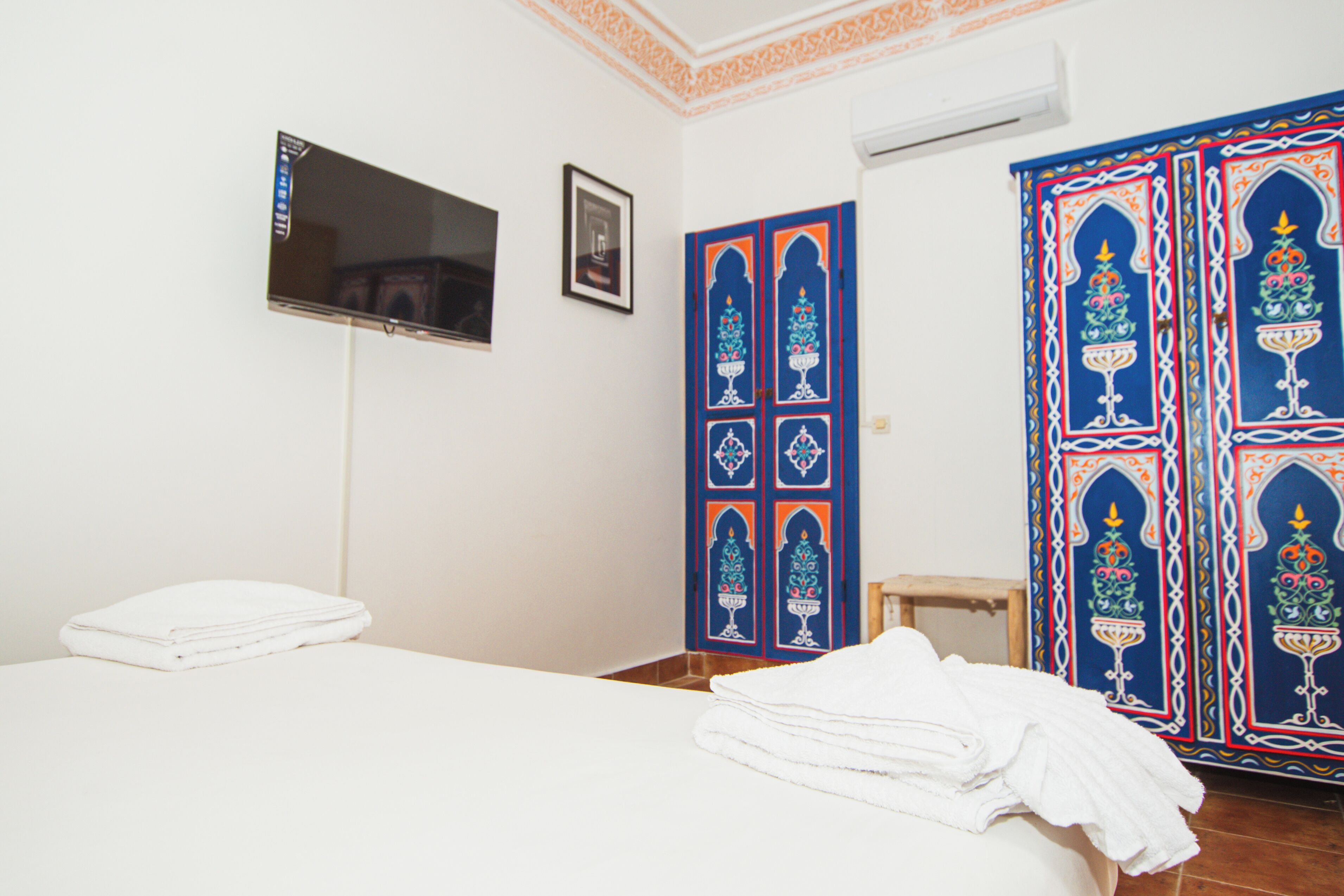 A room with a bed, a TV mounted on the wall, a door with decorative panels, and a wardrobe with intricate designs.