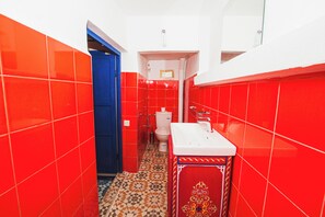 Et badeværelse med røde fliser, en blå dør, et hvidt toilet og en vask med et skab med mønster.