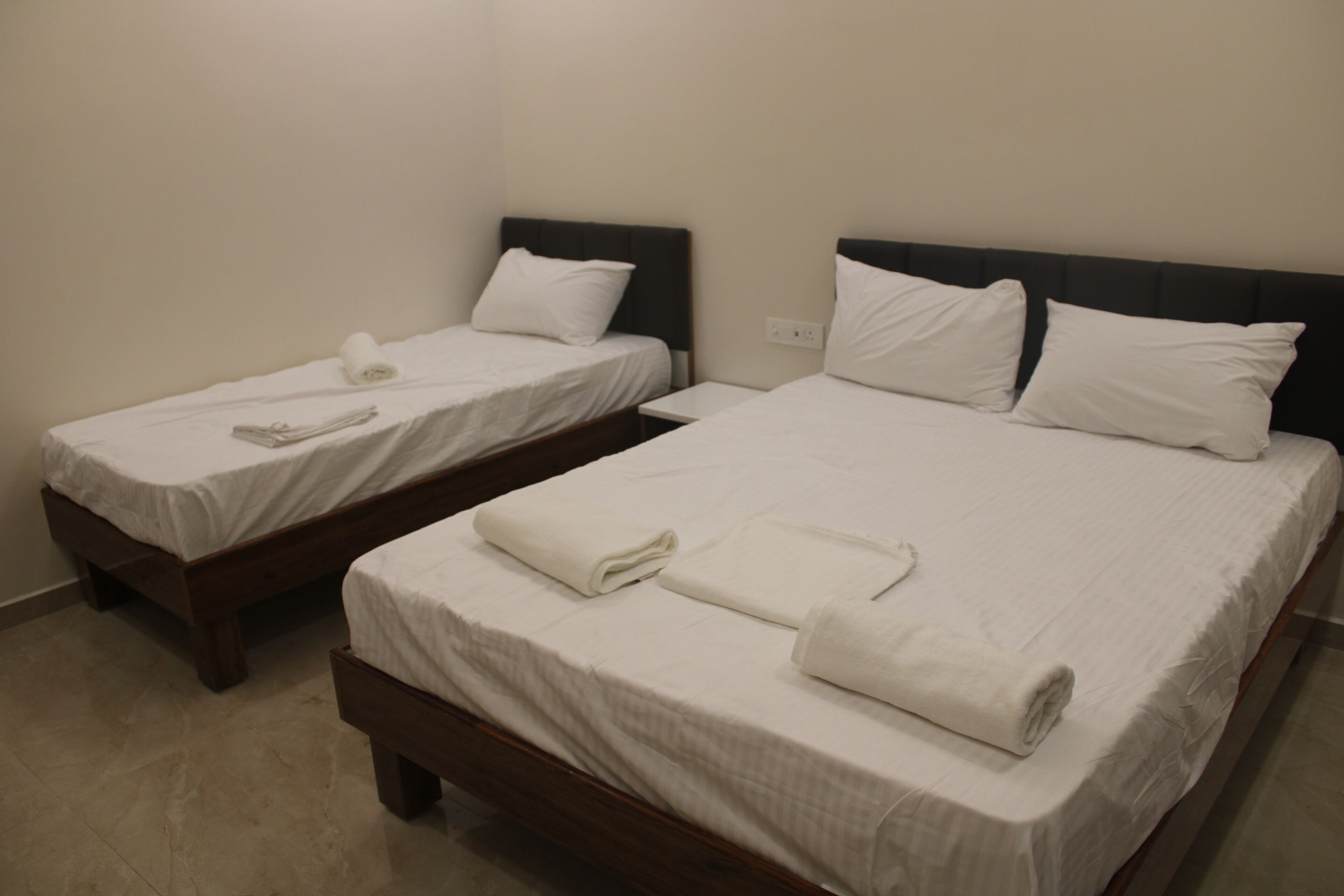 Two single beds with white linens and pillows, a wooden headboard, and a plain wall.