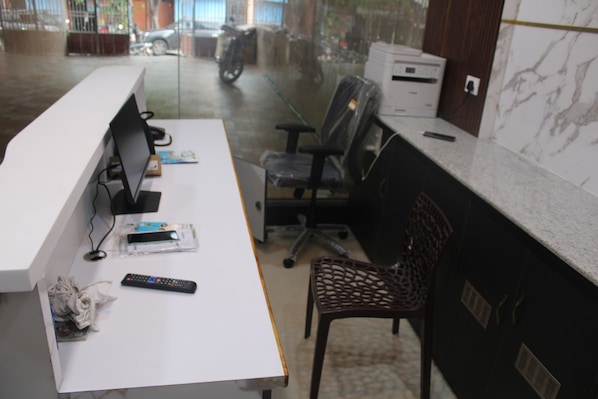 Mostrador de recepción con una computadora, una silla, un control remoto y un objeto envuelto en plástico sobre la mesa.