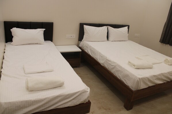 A hotel room with two single beds, each with a wooden headboard, white linens, and a small bedside table. - GRS Inn (Tiruvannamalai)