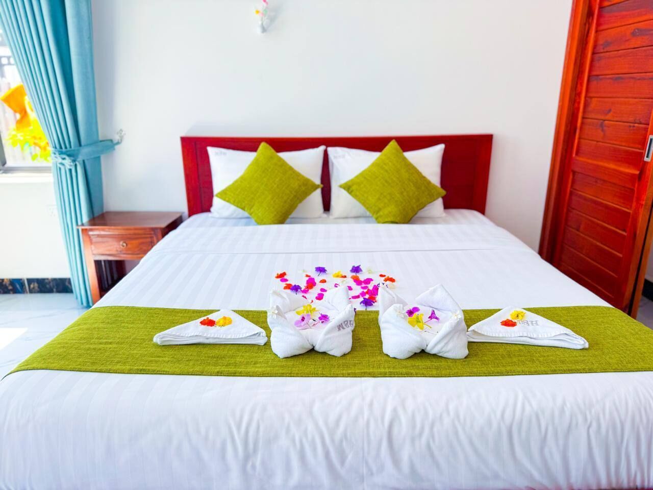 Ein ordentlich bezogenes Bett mit einer grünen Tagesdecke, weißen Laken und dekorativen Handtüchern mit Blumenmotiven.