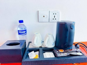 A hotel room's minibar with a bottle of water, two teapots, a coffee maker, and some snacks.