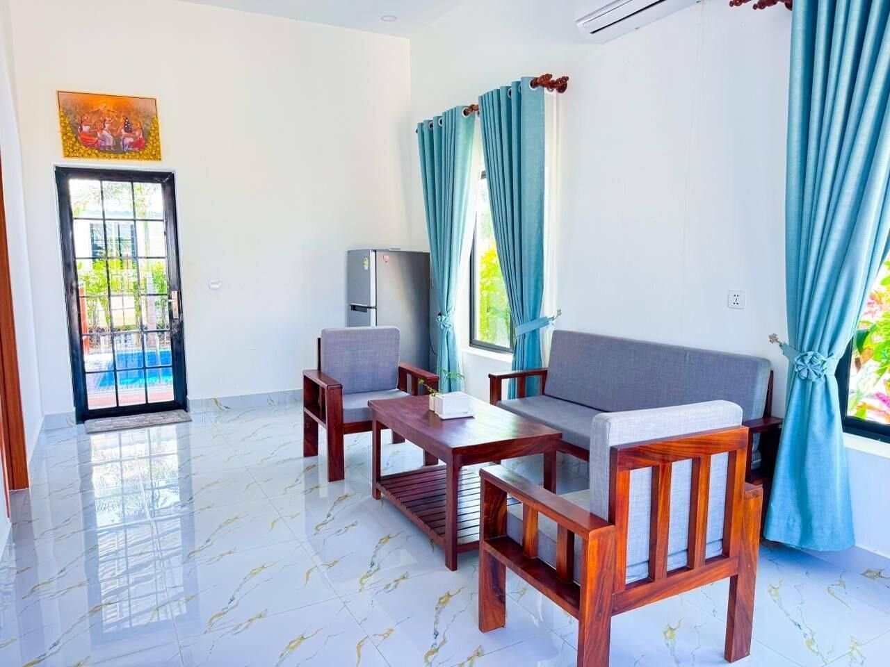 A room with a sofa, two chairs, a small table, a TV, and a window with curtains.